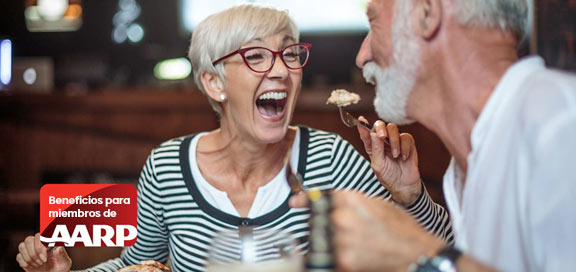 Pareja mayor riéndose en una mesa con el logo de AARP en una esquina